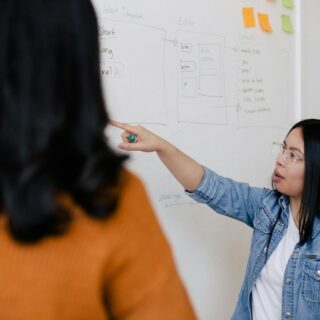 two women standing in front of white dry erase board