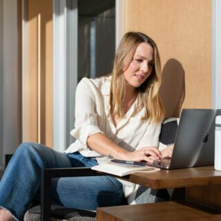 woman in white long sleeve shirt and blue denim jeans sitting on brown wooden table using