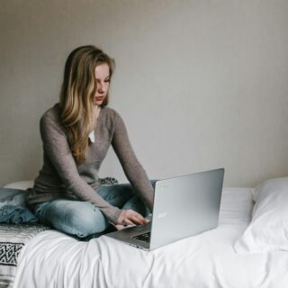 woman typing on MacBook Pro while sitting on bed in room